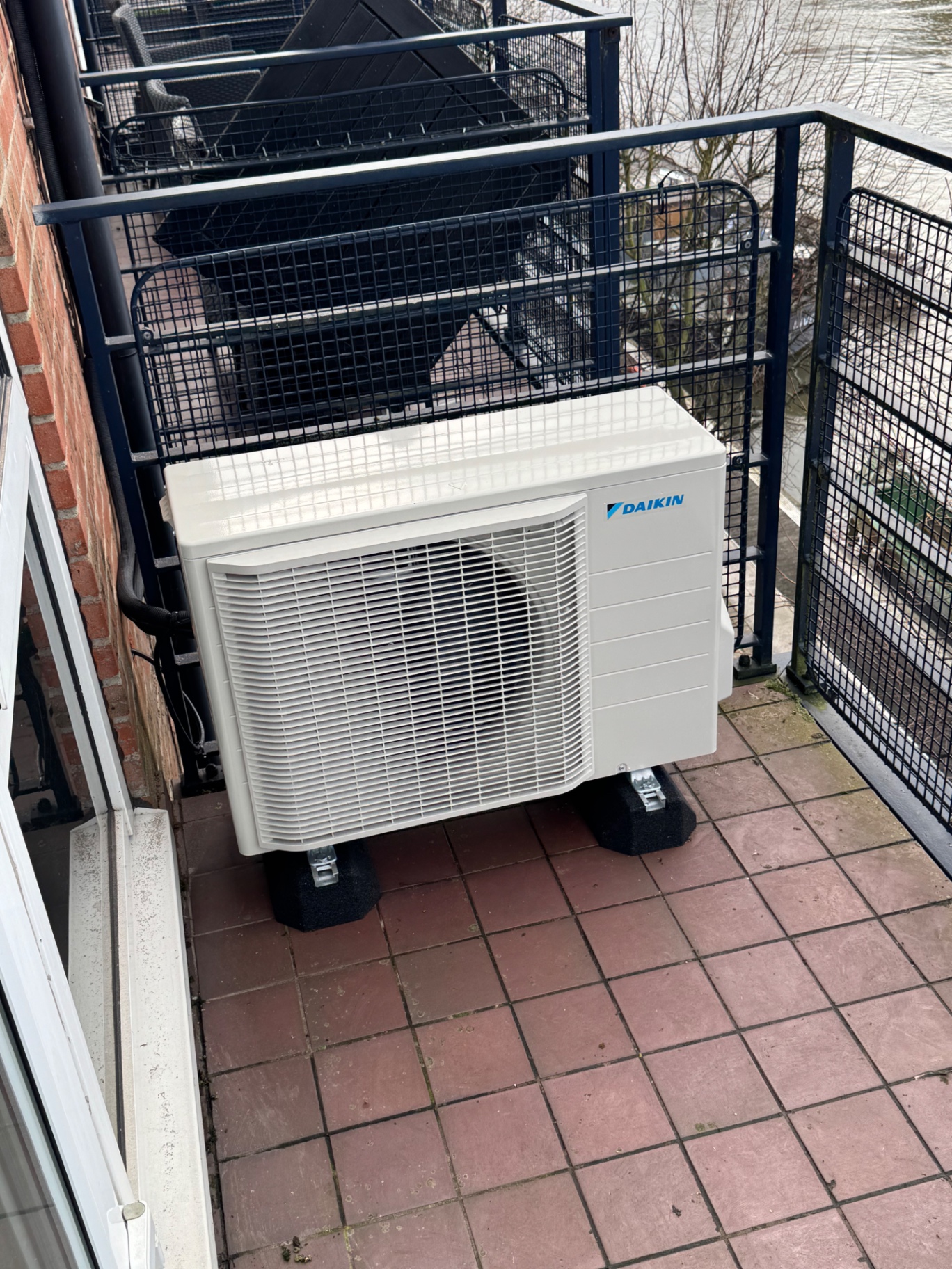 Daikin outdoor air conditioning unit installed on an apartment balcony overlooking the river