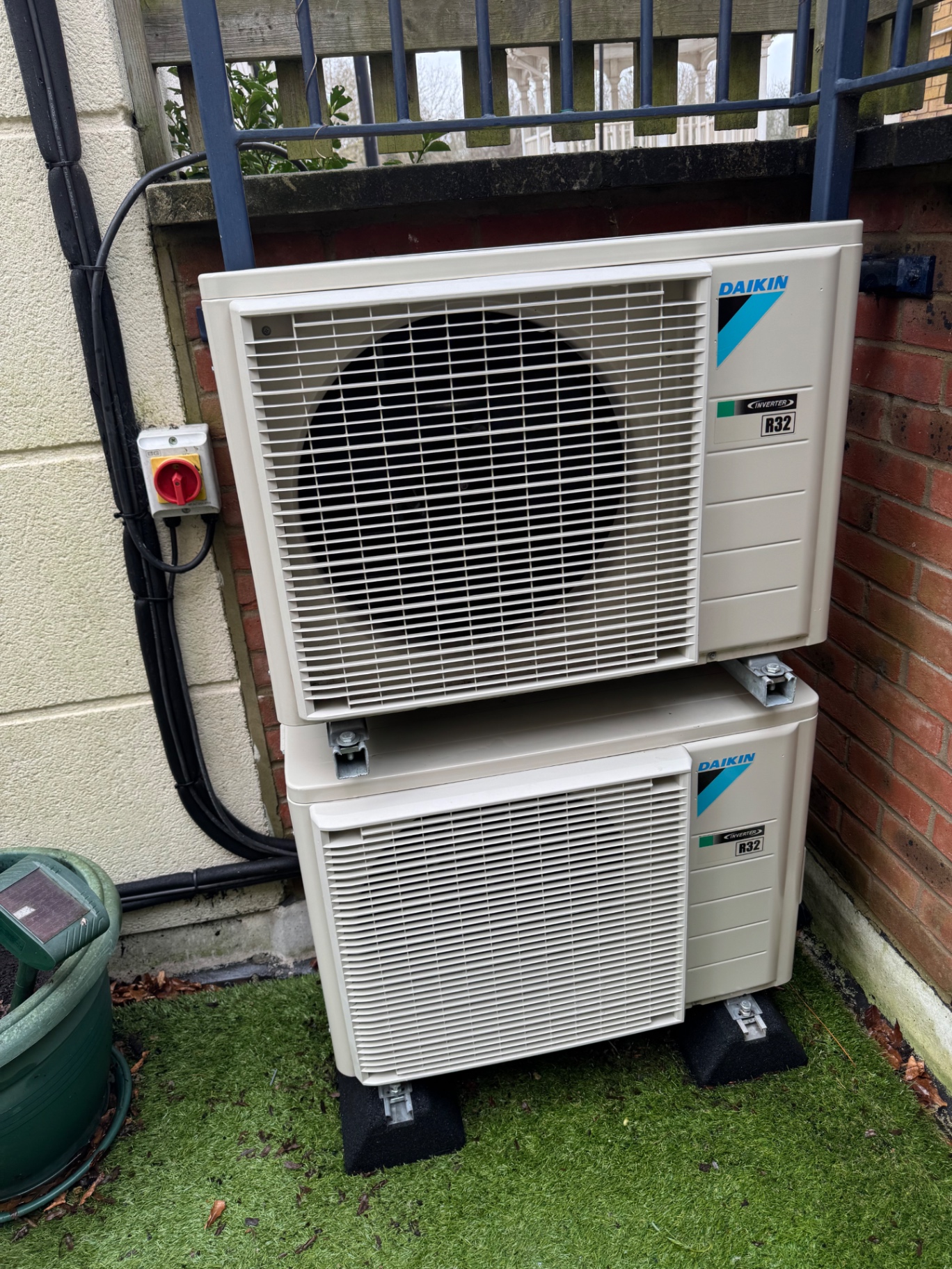 Two stacked Daikin R32 inverter outdoor air conditioning units on anti-vibration pads beside a house in Sutton
